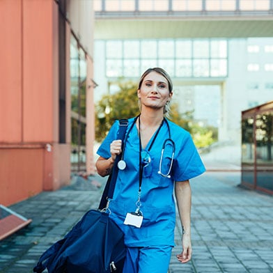 A%20confident%20and%20smiling%20female%20nurse%20wearing%20blue%20scrubs%20is%20walking%20outside%20a%20hospital%20on%20her%20way%20to%20work.%20She%20is%20carrying%20a%20blue%20duffle%20bag%20with%20all%20the%20things%20she%20will%20need%20for%20a%20long%20shift%20at%20work.%20%20