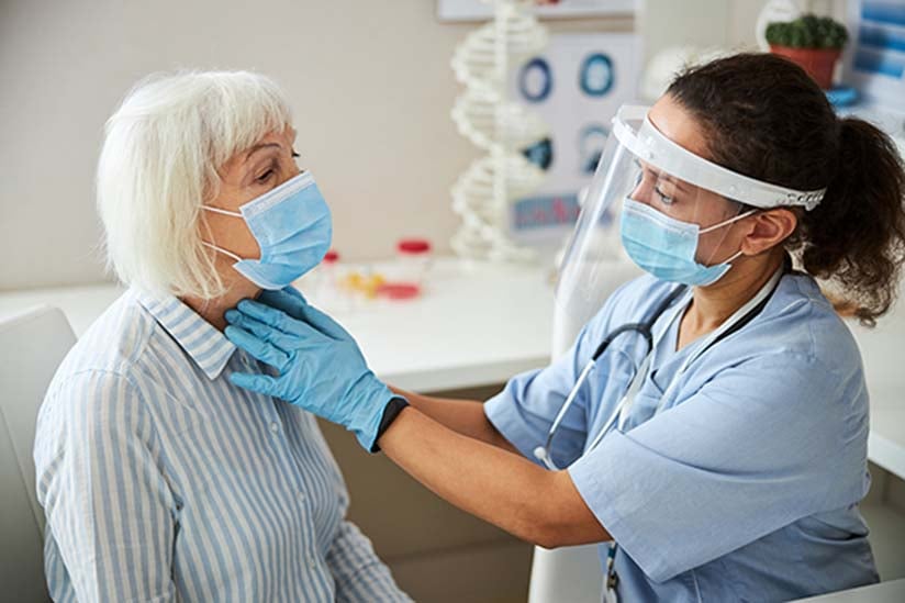 A pediatric nurse in a white coat and mask uses a stethoscope to listen to a young girl's heart, who looks at her with trust and curiosity during a medical check-up in a clinic.