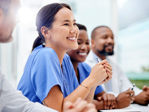 A group of healthcare workers are seated at a long table and discussing ways to improve health. They are smiling and engaged in conversation.