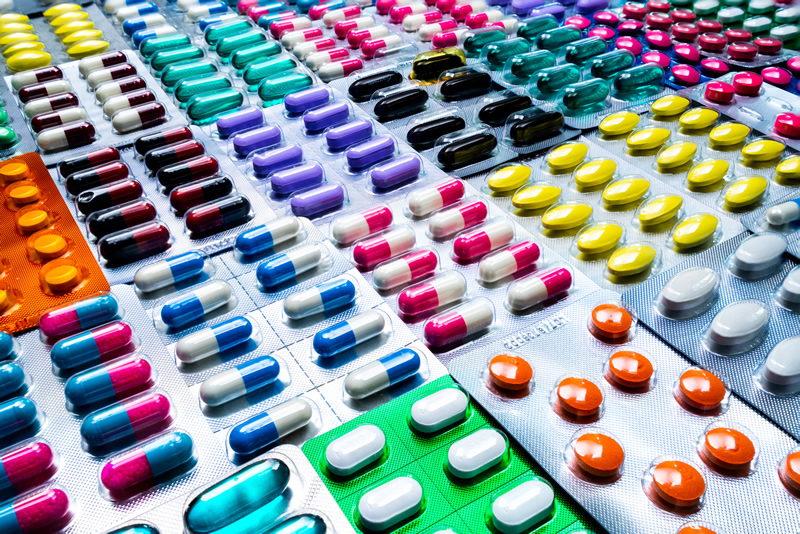 A colorful assortment of various shaped medications in pill blister packs is laying on a surface, creating a collage of colorful pills.