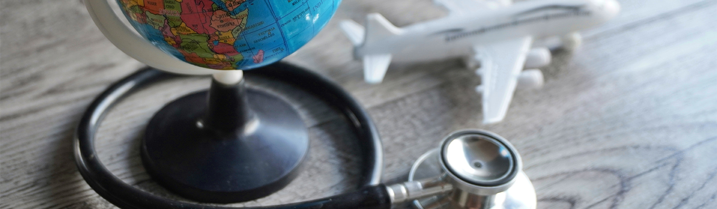 Image of a colorful small globe and a white toy airplane resting on a grey tabletop. There is a stethoscope wrapped around the base of the globe.